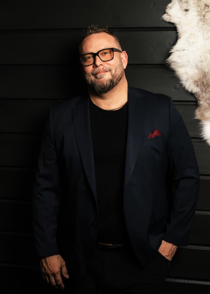 Petri Juotasniemi in a dark blazer against a black timber wall